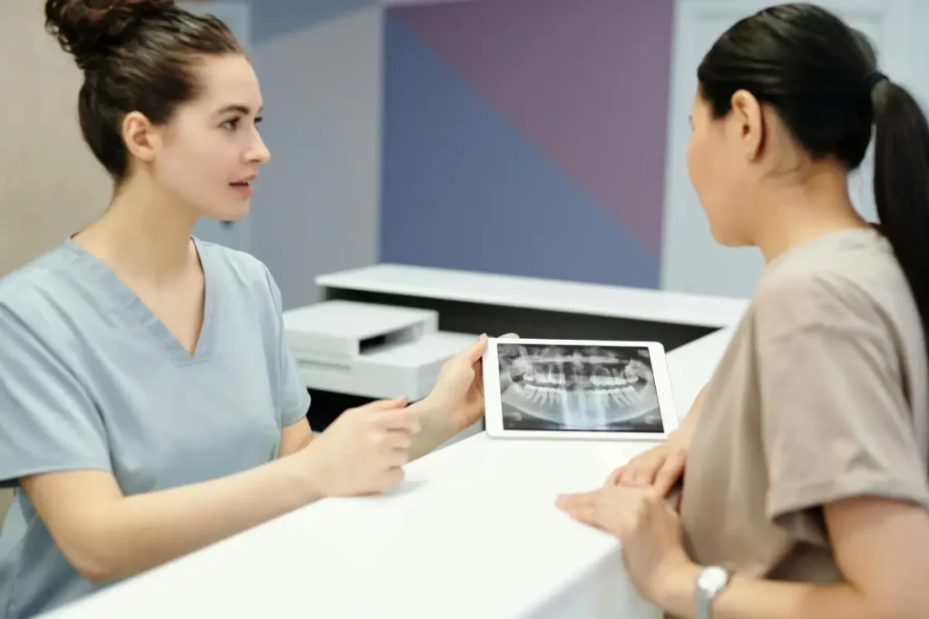 Dental professional in scrubs consulting with a patient using a tablet in a modern clinic